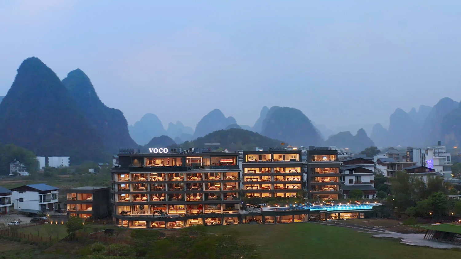 Modern hotel building with illuminated windows against a mountainous landscape at dusk.